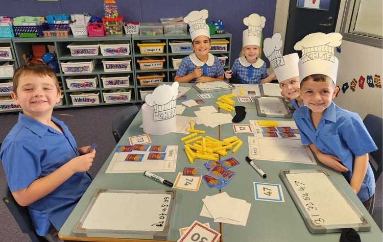 Students sitting together in a group at a table, some have fancy hats on for their learning activity.