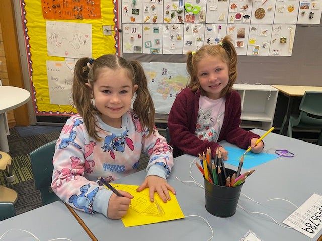 2 girls sitting at a table, smiling and colouring in