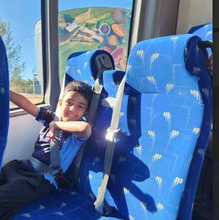 a boy sitting on the bus wearing a seat belt and smiling.