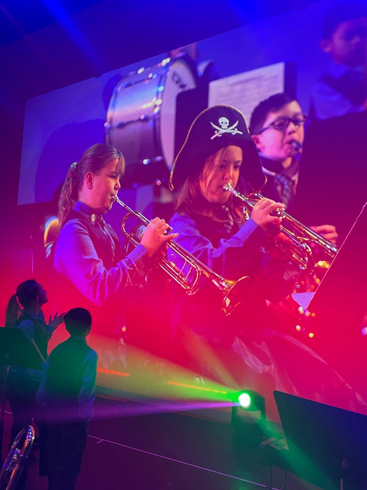 students on stage under lights, playing trumpets